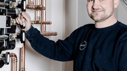 Der Techniker greift an einem Ventil einer Heizungsanlage, während er in einem hellen, gut beleuchteten Raum posiert.