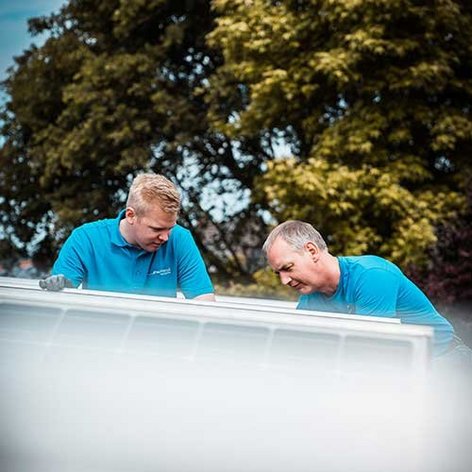 Zwei Männer in blauen T-Shirts arbeiten konzentriert an einer Solaranlage unter einem klaren Himmel.