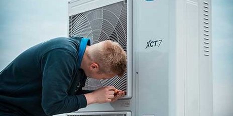 Ein Techniker arbeitet an einer Klimaanlage, konzentriert auf die Wartung des Geräts auf einem Dach.