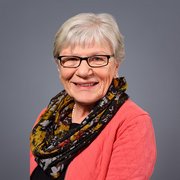 Die Dame mit grauen Haaren und Brille strahlt Lebensfreude aus, während sie in einem eleganten Outfit posiert.