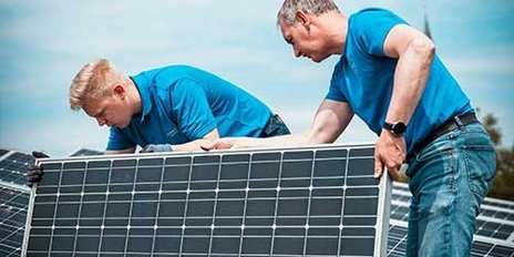 Auf einem Dach arbeiten zwei Männer an der Montage eines Solarpanels, umweltfreundliche Energie im Fokus.