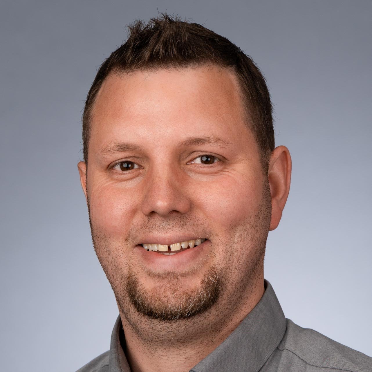 Der Mann hat kurzes, gestyltes Haar und lächelt, während er in die Kamera schaut, was eine positive Ausstrahlung vermittelt.