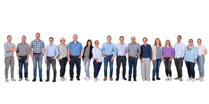 Die Gruppe besteht aus Männern und Frauen unterschiedlichen Alters, die in einer freundlichen Pose zusammenstehen.