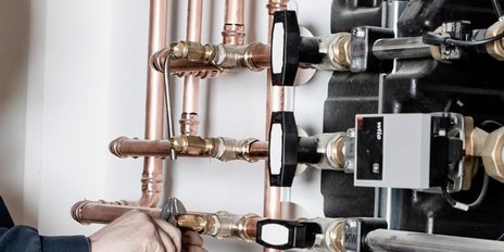 Der Techniker lächelt, während er mit einer Zange an einer Heizungsanlage mit zahlreichen Rohren und Anschlüssen arbeitet.