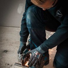 Ein Handwerker kniet auf dem Boden und benutzt eine elektrische Säge, während Funken fliegen und der Raum schwach beleuchtet ist.