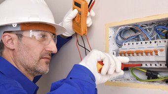 Ein Elektroniker der an einem Sicherungskasten schraubt