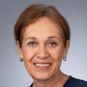 Die Frau trägt ein dunkles Oberteil und hat kleine Ohrringe, während sie in die Kamera lächelt.