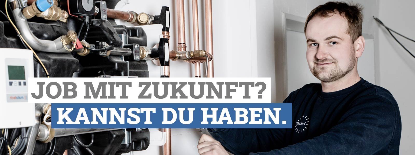Ein junger Mann lächelt, während er an einer Heizungsanlage mit Kupferrohren arbeitet, umgeben von moderner Technik.
